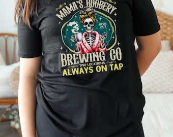 May include: Black t-shirt with a graphic of a skeleton in a pink robe holding a coffee mug. The graphic says "Mama's Boobery Brewing Co. Two Locations Always On Tap" with a skull and crossbones logo.