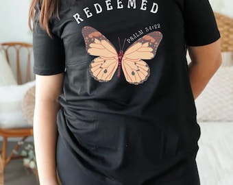 May include: Black t-shirt with the word "REDEEMED" in white lettering and a butterfly graphic. The text "PSALM 34:22" is printed below the butterfly.