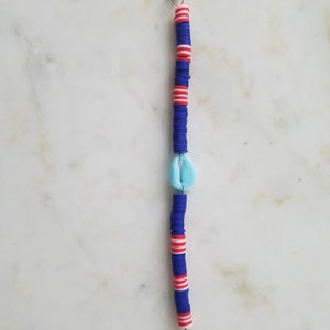 May include: A blue and red beaded bracelet with a white shell charm and silver clasps.