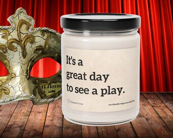 Peut inclure: Un bocal de bougie blanc avec un couvercle noir et une étiquette qui dit "C'est un grand jour pour voir une pièce de théâtre." L'étiquette comprend également le texte "Theatre Verse" et "bougie en soja végane écologique."