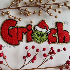May include: Red and gold embroidered patch with the word "Grinch" and a green Grinch character wearing a Santa hat. The patch is on a white background with red and gold berries.
