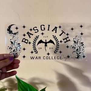 May include: Black and white sticker with the text "Basgiath Fly or Die War College" and a black silhouette of a dragon with wings spread. The sticker is on a clear background with a crescent moon and stars.