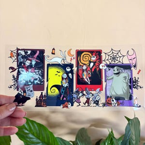 May include: A clear sticker featuring four rectangular panels with characters from The Nightmare Before Christmas. Each panel has a different scene with characters like Jack Skellington, Sally, and Oogie Boogie. The sticker has a light beige background.