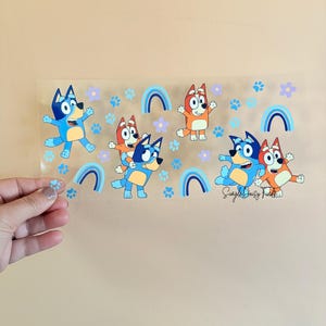 May include: A clear sticker sheet featuring cartoon dogs in blue and orange. The sheet includes paw prints, flowers, and rainbows in blue and purple. The text "Simple Daisy Finds" is visible in the bottom right corner.