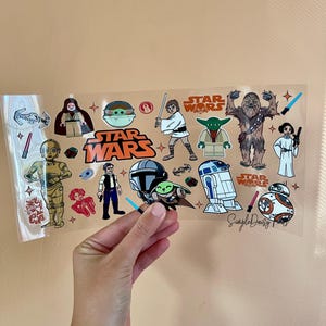 May include: A sheet of clear plastic with Star Wars themed stickers. The stickers feature characters like Yoda, Chewbacca, R2-D2, and BB-8. The stickers are in various colors, including orange, blue, green, and red. The text "Star Wars" is printed in orange on the sheet.