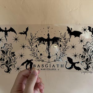 May include: A clear sticker sheet featuring black dragon and bat silhouettes, stars, and floral elements. The text "BASGIATH WAR COLLEGE" is also present. The design has a gothic or fantasy theme.