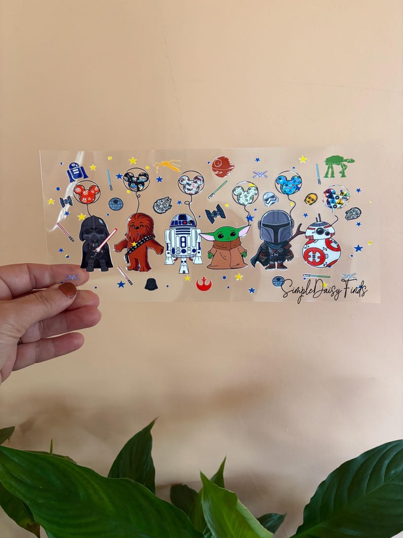 May include: A clear sheet of vinyl with a variety of Star Wars characters and Mickey Mouse. The characters are holding balloons with Mickey Mouse heads on them. The sheet also has stars and other space-themed designs. The text "Simple Daisy Finds" is at the bottom of the sheet.