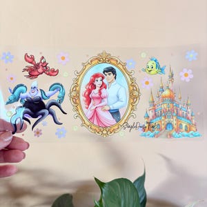 Peut inclure: Un autocollant transparent avec des illustrations de conte de f&eacute;es. Il pr&eacute;sente un portrait d'un couple dans un cadre dor&eacute;, un ch&acirc;teau et des cr&eacute;atures marines. Le texte "Simple Daisy Finds" est &eacute;galement pr&eacute;sent.