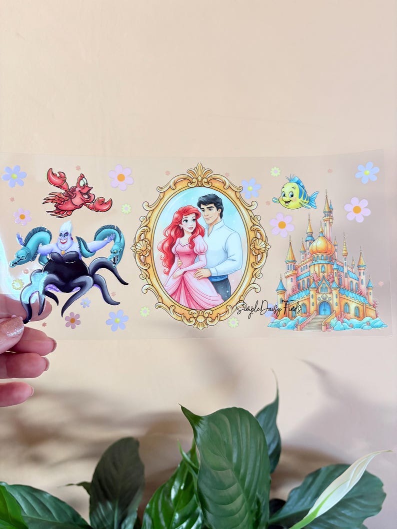Peut inclure: Un autocollant transparent avec des illustrations de conte de f&eacute;es. Il pr&eacute;sente un portrait d'un couple dans un cadre dor&eacute;, un ch&acirc;teau et des cr&eacute;atures marines. Le texte "Simple Daisy Finds" est &eacute;galement pr&eacute;sent.