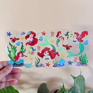 May include: A clear sticker sheet featuring illustrations of a mermaid with red hair, sea creatures, and aquatic plants. The sticker sheet includes the text "Simple Daisy Finds".