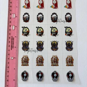 Puede incluir: Una hoja de pegatinas con personajes de Pesadilla antes de Navidad. Las pegatinas incluyen a Sally, Jack Skellington y otros dise&ntilde;os tem&aacute;ticos. Una regla rosa con medidas en pulgadas es visible en el lado izquierdo.