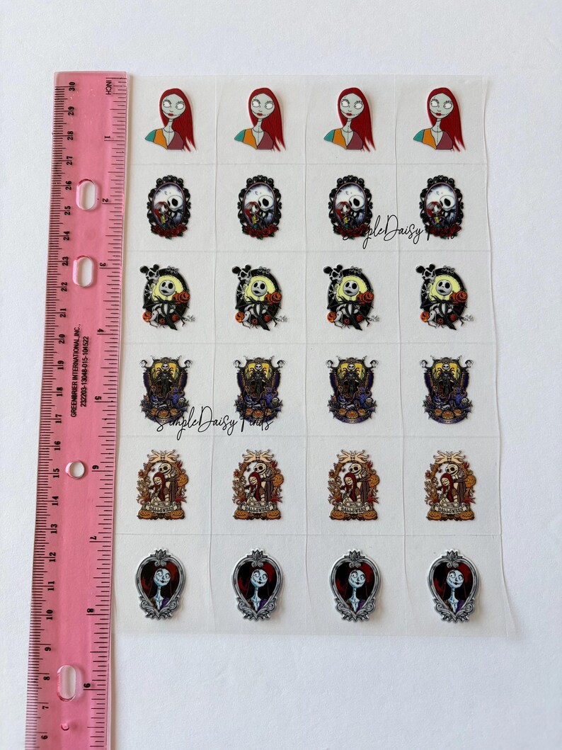 Puede incluir: Una hoja de pegatinas con personajes de Pesadilla antes de Navidad. Las pegatinas incluyen a Sally, Jack Skellington y otros dise&ntilde;os tem&aacute;ticos. Una regla rosa con medidas en pulgadas es visible en el lado izquierdo.