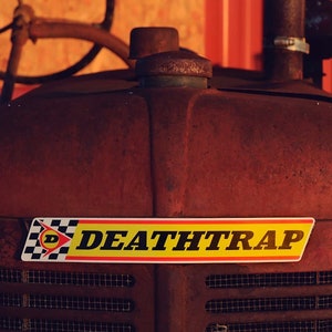 Peut inclure: Un tracteur rouge rouillé avec un autocollant noir et jaune qui dit "DEATHTRAP" à l'avant.
