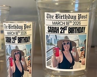 May include: Clear plastic cups with a printed label that reads "The Birthday Post, MARCH 18TH 2026, SARAH 21ST BIRTHDAY." The label features a photo of a woman on a boat. One cup is tall, the other is shorter.