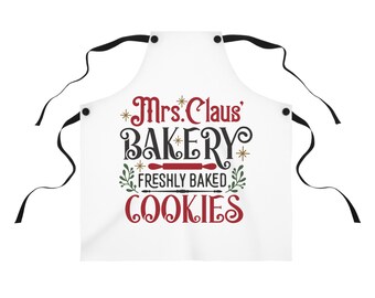 Könnte beinhalten: Weisse Schürze mit schwarzen Bindebändern. Der Text "Mrs. Claus' BAKERY FRESHLY BAKED COOKIES" ist in Rot und Schwarz gehalten. Das Design umfasst eine Teigrolle und Blätterzweige. Ein festliches Küchenzubehör.