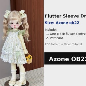 Op de afbeelding: Een pop in een witte jurk met fladderende mouwen, een bloemenpatroon en een groene kraag. De pop heeft blond haar in staartjes met witte strikken. De tekst luidt "Flutter Sleeve Dress" en "Azone OB22".