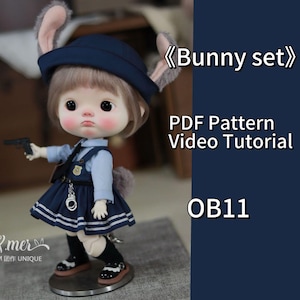 May include: A blue and white bunny outfit for a doll. The outfit includes a hat, a shirt, a skirt, and shoes. The doll is wearing the outfit and is holding a toy gun. The text "Bunny set" and "PDF Pattern Video Tutorial OB11" is visible in the image.