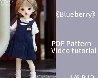 Pode incluir: Uma boneca vestindo um traje azul e branco com um colarinho branco e uma etiqueta com o nome "Dear April". A boneca está usando meias brancas e sapatos pretos. O fundo é de cor roxo claro com o texto "Blueberry", "PDF Pattern Video tutorial" e "1/6 BJD".
