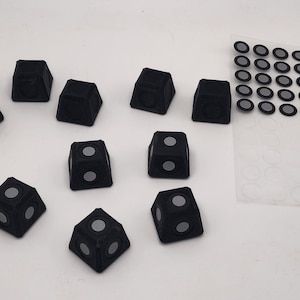 May include: Ten black dice with white dots on each side. The dice are arranged in a semi-circle on a white surface. There is a sheet of clear plastic with black circles on it in the upper right corner of the image.