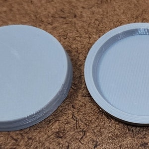 May include: Two gray plastic round lids, one with a smooth top and the other with a slightly raised rim.