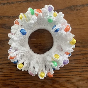 May include: White crocheted hair scrunchie with colorful beads. The beads are in shades of blue, green, yellow, orange, and purple.