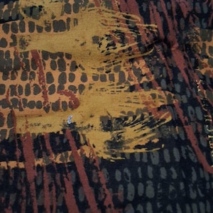 May include: Close-up of a fabric with an abstract design. The fabric features a mix of colors, including shades of brown, orange, and black. The design includes brushstroke-like patterns and dotted textures. The text "ONS DESIGNED BY LONNI ROSSI UNDER LICENSE" is visible.