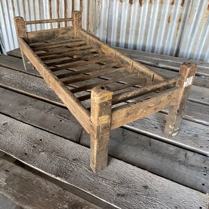 May include: A rustic wooden bed frame with a slatted design. The frame is made of weathered wood and has a simple, farmhouse style.