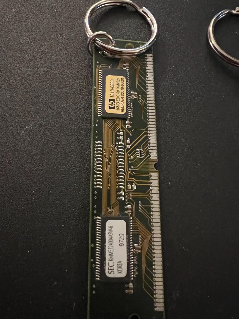 May include: A green circuit board keychain with a silver key ring. The circuit board has a black chip with the text "SEC KMM5324004ASW-6 KOREA 9729" and a smaller black chip with the text "hp 1818-6883 16MB EDO 60 (4Mx32) REORDER D3648-63001".