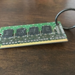 Peut inclure: Une carte de circuit imprimé verte avec un anneau métallique noir attaché. La carte de circuit imprimé a quatre puces noires et des connecteurs dorés.