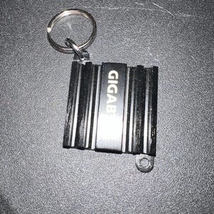 May include: Black metal keychain with a silver ring and the word "GIGAB" engraved on the front.