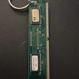 May include: A green circuit board keychain with a silver key ring. The circuit board has text that reads "hp 1818-6883 16MB EDO 60 (4Mx32) REORDER D3648-63001" and "SEC KMM5324004ASW-6 KOREA 9742 H".