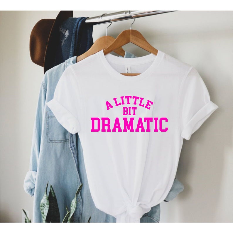May include: White t-shirt with a pink graphic that says "A Little Bit Dramatic".