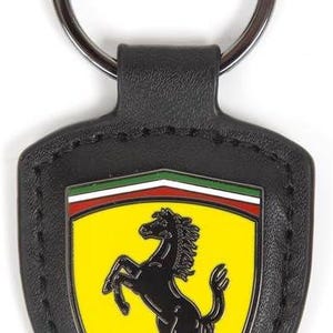 May include: A black leather keyring featuring a shield-shaped emblem with a yellow background, a black prancing horse, the letters SF, and a horizontal green, white, and red stripe at the top, attached to a circular silver metal split ring.