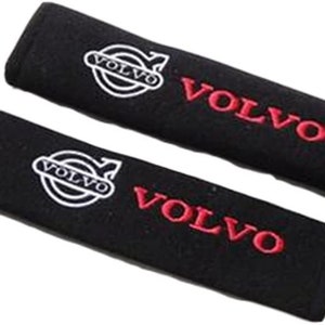 以下が含まれることがあります： 白のボルボのロゴと赤のVOLVOの文字が入った、黒いシートベルトカバーが2つ。カバーは長方形で、柔らかく質感のある素材でできています。