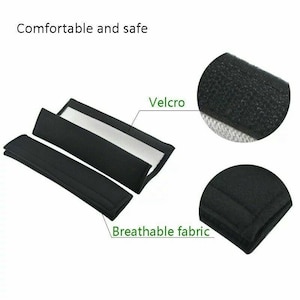 May include: Two black seat belt pads with a white lining and velcro closures. The pads are made of breathable fabric and are designed to provide comfort and safety.