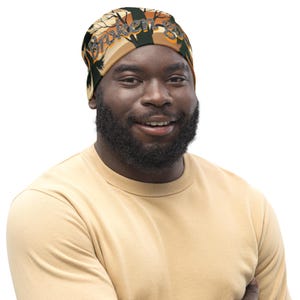 May include: A black and tan bandana with the text "Broken Gods" in orange lettering. The bandana features a tree and branch design. The person in the image is wearing a light yellow crew neck top.