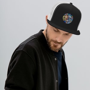 May include: Black trucker hat with a white mesh back and a colorful, abstract design on the front. The design is a circular image with a face-like pattern in shades of blue, green, yellow, and red.
