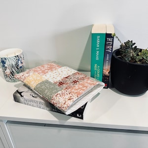 May include: A book cover with a patchwork design in shades of pink, yellow, and green. The cover is lying on top of a book titled "Serpent & Wings - Sight" by  S.J. Broden.  There are two books in the background, one titled "A Court of Mist and Fury" by Sarah J. Maas and the other titled "The Dry" by Jane Harper.