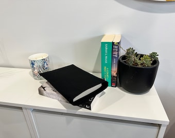 May include: A white shelf with a black book cover, a candle, two books titled "A Court of Mist and Fury" by Sarah J. Maas and "The Dry" by Jane Harper, and a black planter with green succulents.