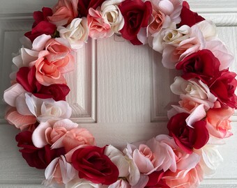 May include: A wreath made of artificial flowers in shades of red, pink, and white. The wreath is made of roses and is perfect for a Valentine's Day or spring decoration.