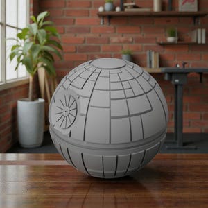 May include: A gray, spherical model of the Death Star from Star Wars. The model features detailed paneling and a circular dish on one side. The sphere is displayed on a wooden surface, with a brick wall and a window in the background.