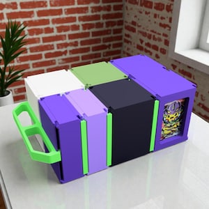 May include: A multi-coloured storage container in shades of purple, white, black, and green. The container features a handle and a design on the side. It is placed on a white surface.