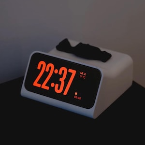 Può includere: Un orologio digitale bianco con un display rosso che mostra l'ora 22:37. L'orologio mostra anche la temperatura, 17°C, e le iniziali ML.