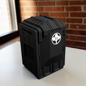 May include: A matte black, rectangular storage container with a textured, mechanical-style exterior featuring recessed panels and vents. A circular white emblem depicting a stylized three-lobed tree icon is centered on the front face of the object.