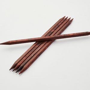 Könnte beinhalten: Satz von sechs Stricknadeln aus Holz, in rotbrauner Farbe mit einer spitzen Spitze. Die Nadeln sind kreuzweise angeordnet.