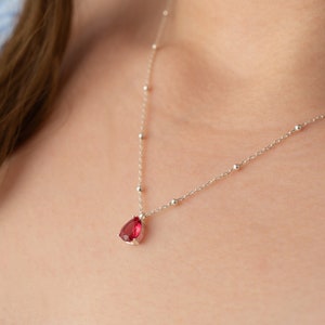 May include: A silver necklace with a small red teardrop-shaped pendant.