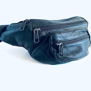 May include: Black leather fanny pack with three zippered compartments. The bag has a ribbed, elasticized strap and silver-toned zipper pulls. The fanny pack is designed to be worn around the waist or across the body.