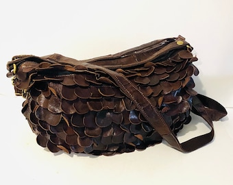 May include: A brown leather shoulder bag with a distinctive petal design. The bag has a long strap and a zip closure. The bag is made of dark brown leather and has gold-coloured hardware.