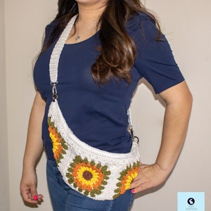 May include: A white crocheted sunflower-themed fanny pack with a long white strap. The bag is worn by a person wearing a blue shirt and blue jeans.