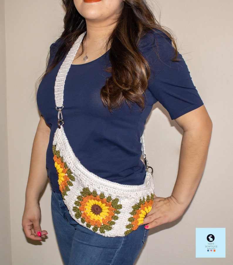 May include: A white crocheted sunflower-themed fanny pack with a long white strap. The bag is worn by a person wearing a blue shirt and blue jeans.